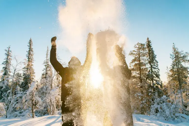 two people throwing snow in the air in a snowy forest