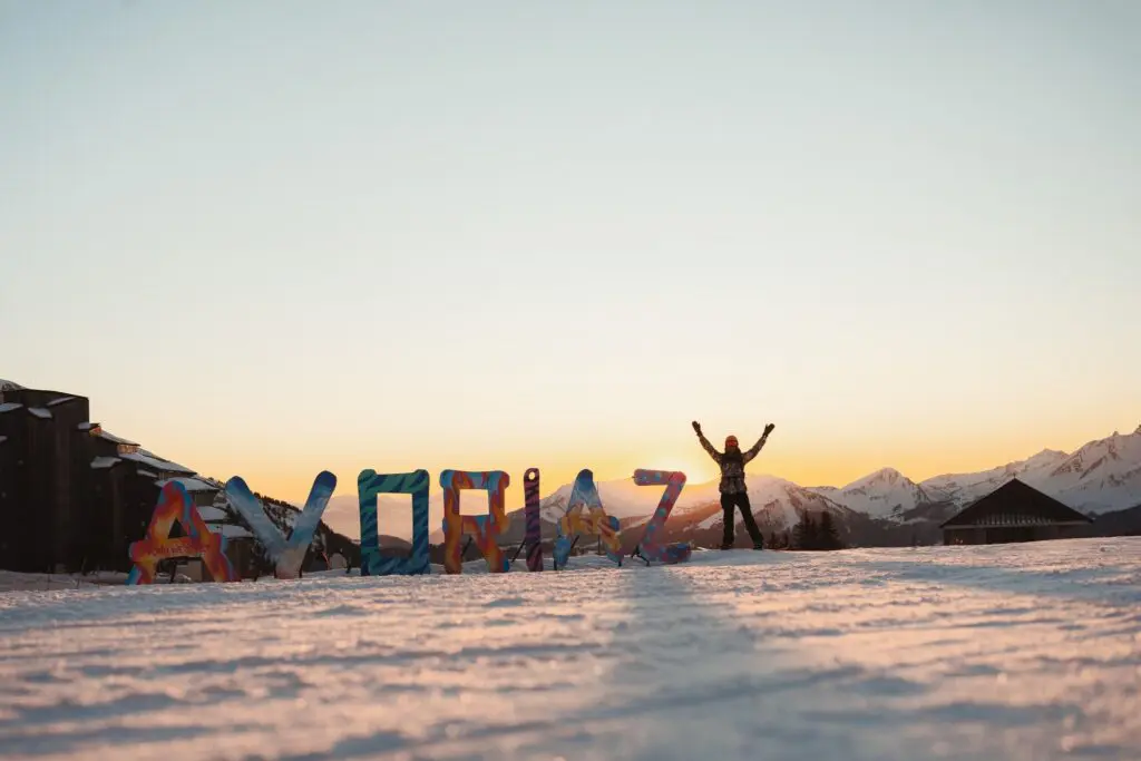 person with arms raised in front of Avoriaz sign at sunset